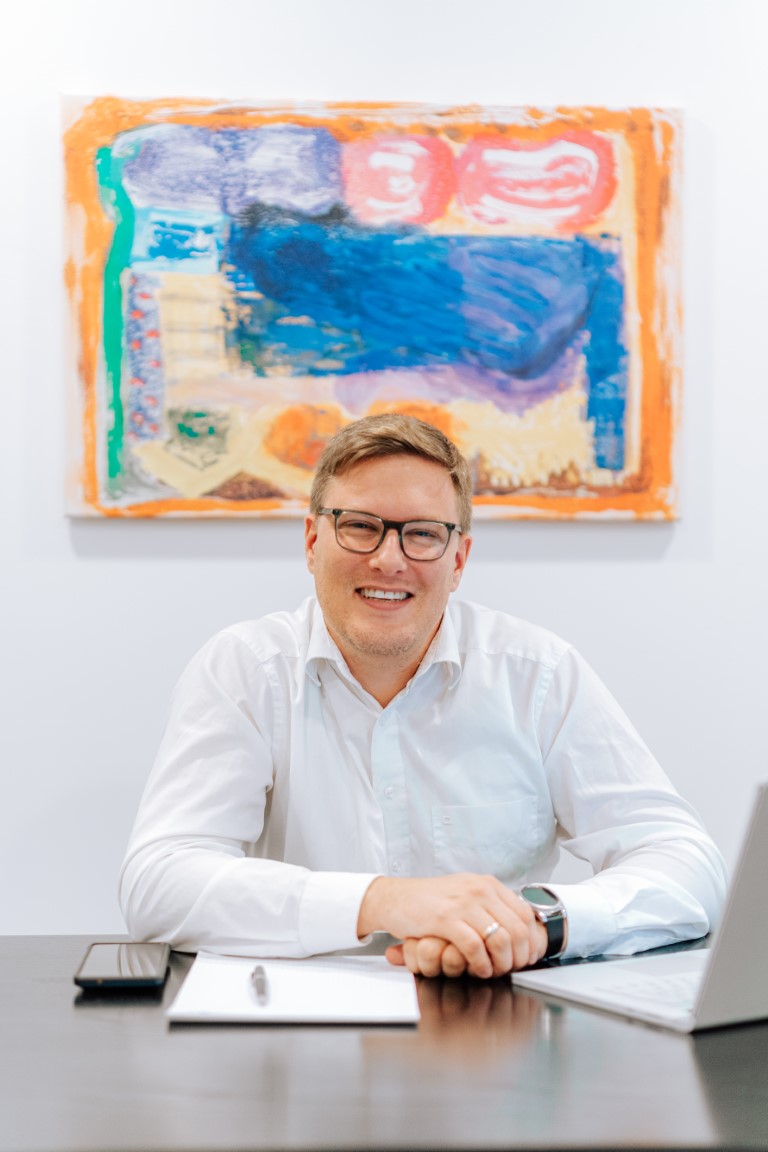 Lächelnder Mann im Büro vor buntem Gemälde